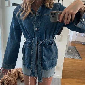 Jeansjacka med bälte i midjan💙 - Snygg jeansjacka i klassisk blå denim med knappar framtill och bälte i midjan för en mer markerad siluett. Jackan har stora fickor framtill och långa ärmar. Perfekt för dig som gillar en avslappnad men trendig look. Köpt från Åhléns med nypris 800kr💙använd fåtal gånger