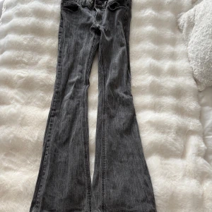 Grå bootcut jeans med utsvängda ben - Snygga grå jeans med bootcut och riktigt utsvängda ben. Jeansen har klassisk femficksdesign och dragkedja fram. Materialet är denim med en tvättad look som ger en cool vibe. Perfekta för dig som gillar retrostil och vill sticka ut.