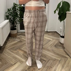 Beige rutiga byxor från lager 157 - Säljer ett par superbekväma beige och vita rutiga byxor från lager 157. De har elastisk midja med snörning och avslappnad passform. Perfekta för chill dagar eller när du vill ha något mjukt och luftigt på dig. Materialet känns lätt och skönt mot huden.