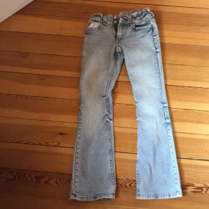 Ljusblå bootcut jeans H&M stl 152 - Snygga ljusblå bootcut jeans från H&M i storlek 152. Jeansen har låg midja, justerbar midja och klassiska bakfickor med lock och knapp. Tillverkade i bomullsmix med lite stretch för extra komfort.