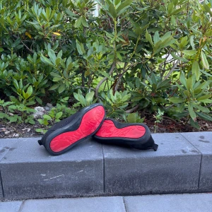 Christian Louboutin svarta sneakers - Säljer ett par svarta sneakers från Christian Louboutin med ikoniska röda sulor och diskret logga undertill. Skorna har snörning, rund tå och är tillverkade i skinn och textil. Kommer med originalkartong och dustbag. Perfekta för dig som vill sticka ut med exklusiv streetstyle.