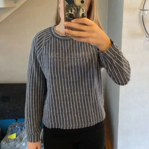 Randig blå tröja från Gina Tricot - Mysig långärmad tröja från Gina Tricot i marinblått med vita vertikala ränder. Tröjan har rund halsringning och en relaxed passform, perfekt för chill dagar. Tillverkad i mjuk bomullsmix som känns skön mot huden.💙