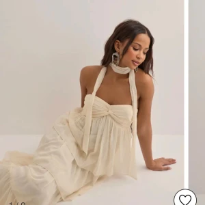 Champagnefärgad långklänning från Nelly - OBS ALDRIG ANVÄNT! Drömmig långklänning från Nelly i champagnefärgad, tunn och flowy polyester. Klänningen har volangiga lager, bandeau-topp med knyt fram och är axelbandslös. Perfekt för sommarens alla tillfällen när du vill känna dig extra fin.