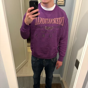 Lila sweatshirt från Index International - Säljer en lila sweatshirt från Index International med tryck på bröstet i rosa och grått.