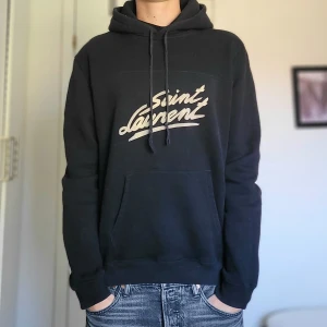 Saint Laurent hoodie - Extremt fet Saint Laurent hoodie! Fint begagnat skick! Nypris 8000, OBS äldre modell utan metallbitar på snören (se sista bild) Äkthetsbevis finns!