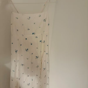 Ljusblommig långklänning med smala axelband - Superfin långklänning i ljus färg med små blå blommor och smala axelband. Klänningen har en feminin passform, knytning i ryggen och är perfekt för varma dagar. Tunt, flowy material som känns luftigt och somrigt.