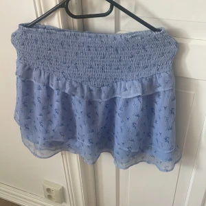 Blå blommig volangkjol Gina Tricot - En blå fin, volang kjol från Gina tricot Young. Använd 2 gånger.