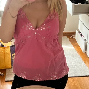 Rosa linnetopp med paljetter och spets - Säljer en söt rosa linnetopp med djup v-ringning, dekorerad med paljetter och broderade spetsdetaljer längs halsringning och nederkant. Tunn och luftig, perfekt för varma dagar eller när du vill känna dig extra fin och med öppen rygg💓