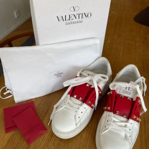 Valentino Rockstud sneakers vit/röd - Säljer dessa Valentino Rockstud sneakers. Köpta oanvända från Vestire Collective som garanterat äktheten. Skon är använd med omsorg och inga nitar saknas, men defekter förekommer (se bild 3 och 4, bild 4 syftar på att skon är ”insjunken”). Box, dustbag, extra nit samt ”kort” medkommer. Det är bara att höra av sig vid frågor!