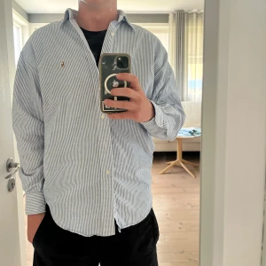 Randig skjorta från Ralph Lauren - Säljer en klassisk blå- och vitrandig skjorta från Ralph Lauren i 100% bomull. Skjortan har långa ärmar och en broderad logotyp på bröstet. Perfekt för en stilren look! Skjortan är i väldigt bra skick och knappast använd. Bara att höra av sig vid eventuella frågor!☺️