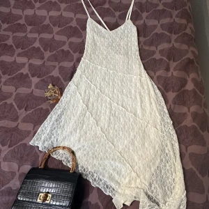 Vit spetsklänning från Bik Bok - Superfin vit långklänning från Bik Bok med tunna axelband och v-ringning. Klänningen har ett lager av spets över ett slätt tyg och asymmetrisk nederkant som ger en flowy känsla. Perfekt för sommarens alla tillfällen när du vill känna dig extra söt.