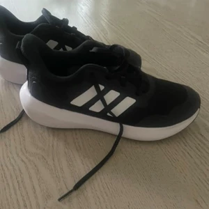 Svarta Adidas sneakers med vit sula - Snygga svarta Adidas sneakers med klassiska vita ränder på sidan och en chunky vit sula. Ovandelen är i mesh och syntet för bra andningsförmåga och komfort. Perfekta för dig som gillar sportig stil och vill ha ett par lätta skor till vardagen. Namn är överstruket med svart penna på undre delen av sulan