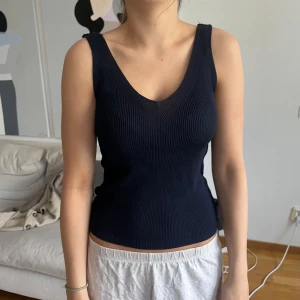 Mörkblå ribbad linnetopp - Snygg mörkblå ribbad linnetopp med breda axelband och v-ringning. Toppen är figurnära och har en stilren, enkel design som passar perfekt till jeans eller kjol. Materialet är stretchigt och bekvämt, vilket gör den lätt att bära hela dagen.