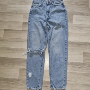 Ljusblå vintage jeans från Gina Tricot  - Ljusblå vintage jeans med slitningar och hål på ena benet. Klassisk femficksmodell med hög midja och raka ben. Jeansen har en avslappnad passform och är tillverkade i bomullsdenim. Perfekta för en chill och trendig look.