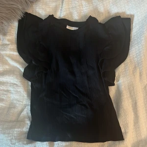 Svart blus med volangärmar Gina Tricot - Supersnygg svart blus från Gina Tricot med breda volangärmar och ribbat tyg. Den är använd en gång och är i storlek 158/164 från Gina Young!💕💕
