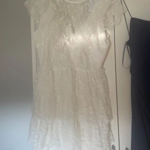 Vit spetsklänning - INTRESSEKOLL!! En fin vit spetsklänning med volanger och korta ärmar. Klänningen har en omlott-design och är en perfekt studentklänning.. Den är tillverkad i ett lätt och luftigt material som ger en luftig känsla. Nypriset är 900 och jag tänker mig 700 kr för den.