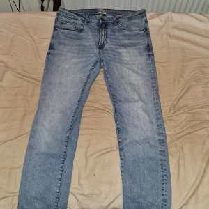 Blå jeans från Dressmann - Säljer ett par blå jeans från Dressmann i slim fit. De har en klassisk femficksdesign och stängs med dragkedja och knapp. W33 och L30. Perfekta för en stilren look.