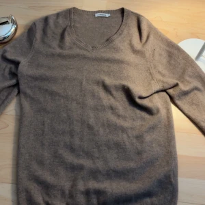 Beige kashmirtröja från J Lindeberg  - Säljer en mjuk och stilren beige kashmirtröja från J Lindeberg. Tröjan har en v-ringad design och långa ärmar, perfekt för kyligare dagar. Den är tillverkad i 100% kashmir vilket ger en lyxig känsla. Passar utmärkt för både vardag och mer uppklädda tillfällen. L men passar M/S
