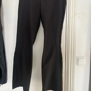 Svarta kostym från BikBok - Snygga svarta kostym från BikBok med en klassisk design. De har en dragkedja framtill och är perfekta för en stilren look. Byxorna har en rak/bootcut passform och är tillverkade i ett bekvämt material. De är midwaist.