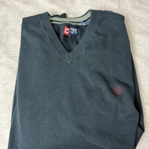 Mörkgrå ärmlös tröja från Chaps - Säljer en stilren mörkgrå ärmlös tröja från Chaps med v-ringning. Tröjan har en broderad logotyp på bröstet och ribbad kant vid halsen. Perfekt för lager-på-lager-stil eller som den är.