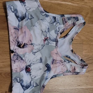 Blommig sporttopp från SOC - Säljer en blommig sporttopp från SOC i mjukt och stretchigt material. Toppen har ett vackert blommönster i rosa och grå toner. Perfekt för träning eller en aktiv dag. Storlek 170 men passar även XS/S.