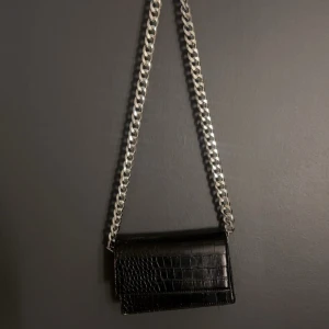 Svart axelväska med kedja - Snygg svart axelväska i skinn med mönster.