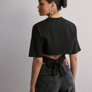 Svart croppad topp med knyt från Nelly🩷 - Snygg svart croppad topp med knyt i ryggen. Toppen har korta ärmar och en stilren design som passar perfekt till både fest och vardag.