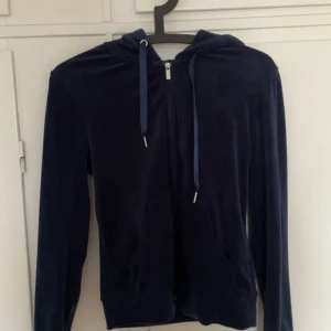 Mörkblå sammetshoodie - Säljer en stilren mörkblå hoodie i mjukt sammetstyg. Den har en dragkedja framtill och justerbara snören i huvan. Perfekt för en avslappnad look.