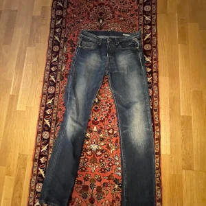 Blå jeans från Replay - Snygga blå jeans från Replay med en klassisk femficksdesign och knappgylf. De har en lätt tvättad look som ger en avslappnad stil. Perfekta för en casual outfit.