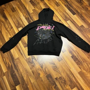 Svart spider hoodie  - Säljer min spider hoodie med en design. Den har en stjärndetalj på baksidan och färgstänk på ärmarna. Perfekt för en avslappnad stil.