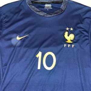 Blå fotbollströja från Nike - Säljer en blå fotbollströja från Nike med nummer 10 och namntryck på ryggen. Tröjan har korta ärmar och FFF-logga på bröstet. Perfekt för fotbollsfans!☀️☀️☀️