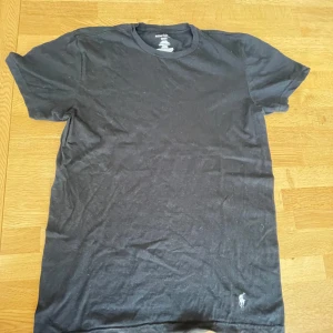 Svart t-shirt från Ralph Lauren - Säljer en klassisk svart t-shirt från Ralph Lauren med broderad logga i vitt på bröstet. T-shirten är tillverkad i 100% bomull och har en normal passform. Perfekt för en stilren och avslappnad look.