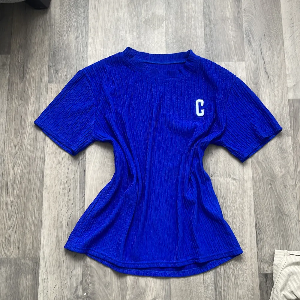 Säljer en snygg blå ribbad t-shirt med en vit bokstavsdetalj på bröstet. T-shirten har korta ärmar och en bekväm passform. Perfekt för en avslappnad stil! Den är ganska stretchig och är one size! . T-paidat.