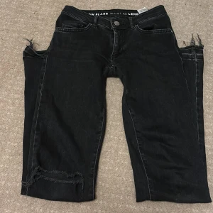 Svarta jeans med flare - Snygga svarta jeans med låg midja och flare-stil. De har en cool slitning vid knäet och fransiga kanter vid bensluten. Perfekta för en trendig look!