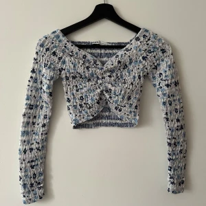 Mönstrad croppad topp från Zara - Säljer en superfin croppad topp från Zara med ett unikt mönster i blått, svart och vitt. Toppen har långa ärmar och en omlott-design framtill som ger en snygg detalj. Perfekt för att piffa upp garderoben!