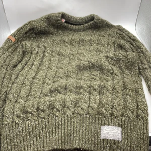 Grön stickad tröja från Superdry - Säljer en olivgrön stickad tröja från Superdry. Tröjan har ett snyggt kabelstickat mönster och ribbade muddar vid ärmslut och nederkant. Perfekt nu när våren kommer.