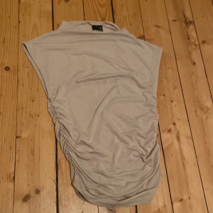 Beige topp från Gina Tricot - Säljer en stilren beige topp från Gina Tricot i storlek XS. Toppen har en draperad design på sidan och är ärmlös, vilket ger en elegant look. Perfekt för olika tillfällen! 💕