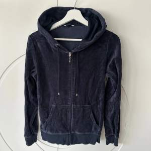 Säljer en snygg mörkblå hoodie med dragkedja och huva. Tröjan har långa ärmar och är tillverkad i ett mjukt material som liknar velour. Perfekt för en avslappnad stil. Den har också praktiska fickor framtill.