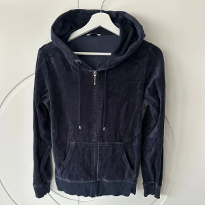 Mörkblå hoodie med dragkedja - Säljer en snygg mörkblå hoodie med dragkedja och huva. Tröjan har långa ärmar och är tillverkad i ett mjukt material som liknar velour. Perfekt för en avslappnad stil. Den har också praktiska fickor framtill.