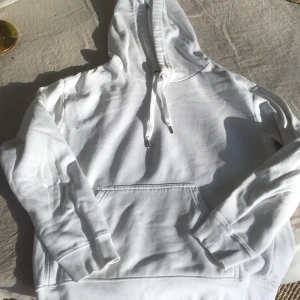 Vit hoodie i storlek XS - Säljer en klassisk vit hoodie med justerbar huva och känguruficka framtill. Perfekt för en avslappnad stil. Passar bra till både jeans och mjukisbyxor.