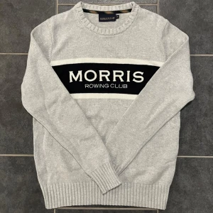Grå tröja från Morris - Säljer en stilren grå tröja från Morris med texten 'Morris Rowing Club' i svart och vitt på bröstet. Tröjan har en rund halsringning och ribbade muddar vid ärmslut och nederkant. Perfekt för en avslappnad och snygg look.