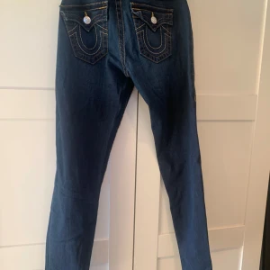 Mörkblå jeans från True Religion - Snygga mörkblå jeans från True Religion med ikoniska bakfickor och kontrastsömmar. Jeansen har en klassisk femficksdesign och knappgylf. Skicket är väldigt bra som nya. 