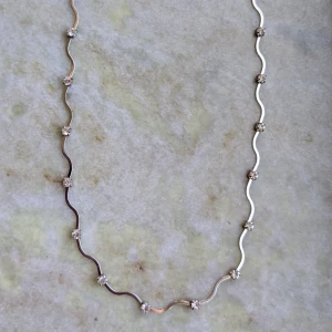 Elegant halsband med vågig design - Snyggt halsband med en unik vågig design. Halsbandet har små glittrande detaljer som ger en extra touch av elegans. Perfekt för att lyfta vilken outfit som helst.
