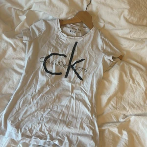 Vit t-shirt från Calvin Klein Jeans - Säljer en stilren vit t-shirt från Calvin Klein Jeans med det ikoniska 'ck' trycket i svart på framsidan. Perfekt för en casual look. T-shirten är kortärmad och gjord i mjukt bomullsmaterial. Inga defekter men lite använd 