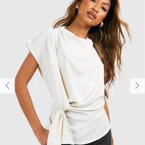 Vit blus med knyt - Elegant vit blus med korta ärmar och knyt i sidan. Perfekt för en stilren look. Blusen har en lös passform och är tillverkad i ett mjukt material som ger en skön känsla.