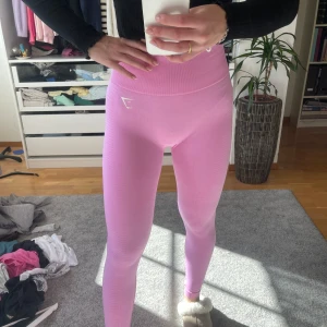 Rosa leggings från Gymshark - Säljer ett par snygga rosa leggings från Gymshark i storlek M. De är tillverkade av en mjuk och stretchig nylonblandning, perfekt för träning eller en aktiv vardag. Högmidjade med en tight passform som framhäver figuren. Aldrig använd