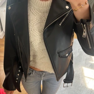 Svart skinnjacka från Zara - Snygg svart skinnjacka från Zara med dragkedja och knappar. Jackan har en klassisk bikerstil med detaljer som bälte och fickor. Perfekt för en cool look.