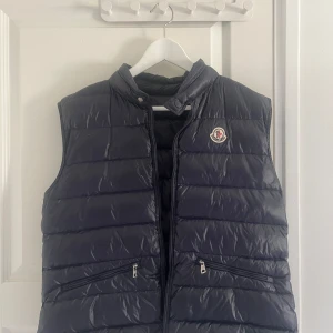 Moncler gui väst - Snygg svart dunväst från Moncler med dragkedja och två fickor framtill. Västen har en klassisk quiltad design och Moncler-logga på bröstet. Perfekt för kyligare dagar och varmare dagar när du vill hålla stilen. NFC-chippet fungerar som det ska. Kvitto finns tyvärr inte kvar då det har slängts. Vid frågor – skicka gärna ett meddelande privat!
