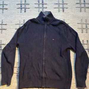 Mörkblå ribbad tröja från Tommy Hilfiger - Säljer en stilren mörkblå ribbad tröja från Tommy Hilfiger. Tröjan har en dragkedja framtill och en liten logotyp på bröstet. Perfekt för en avslappnad och snygg look. Skickt 7/10