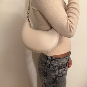 Beige axelväska i syntet - Snygg beige axelväska i syntetmaterial med en stilren design. Väskan har en praktisk dragkedja och en justerbar axelrem. Pris går att diskuteras